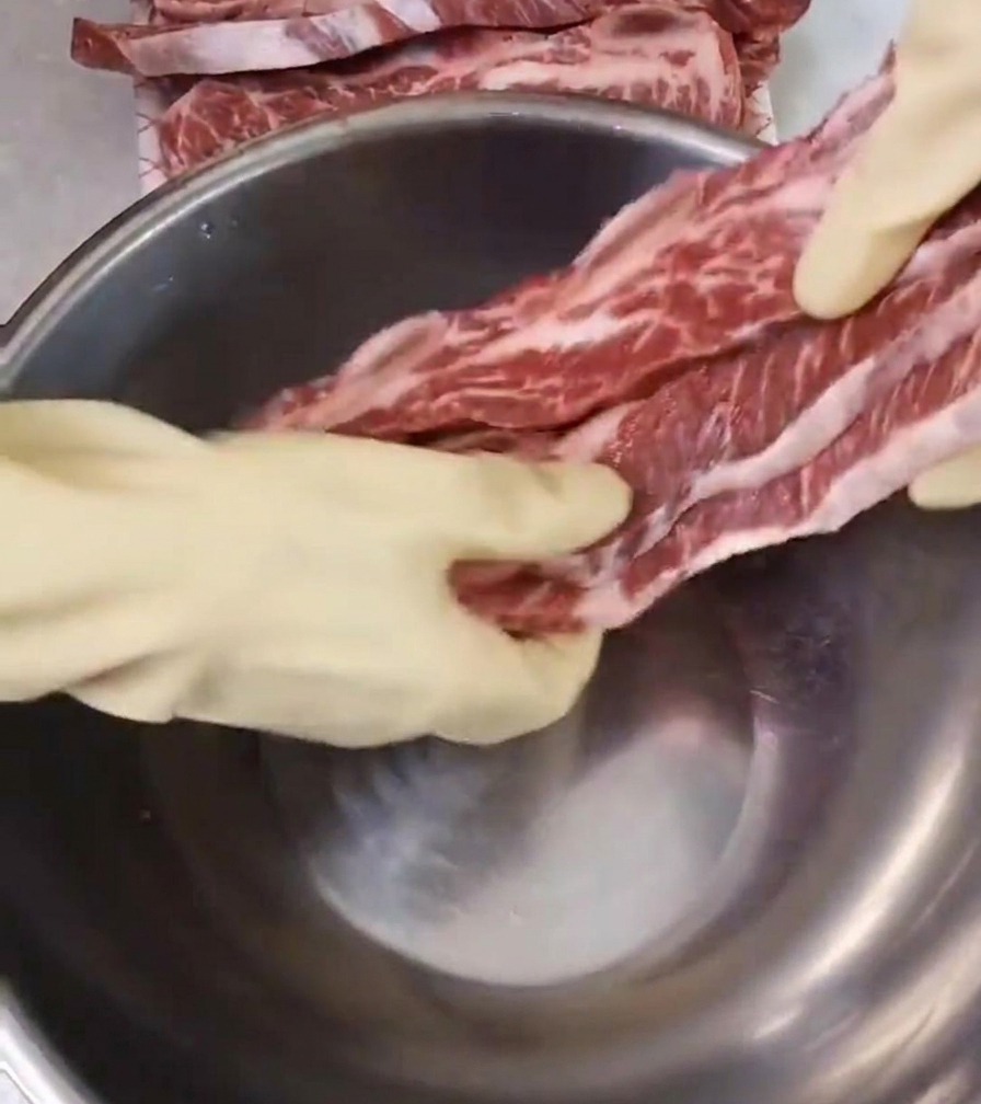 Costine di manzo crude e marmorizzate poste in una ciotola capiente di acciaio inox.
