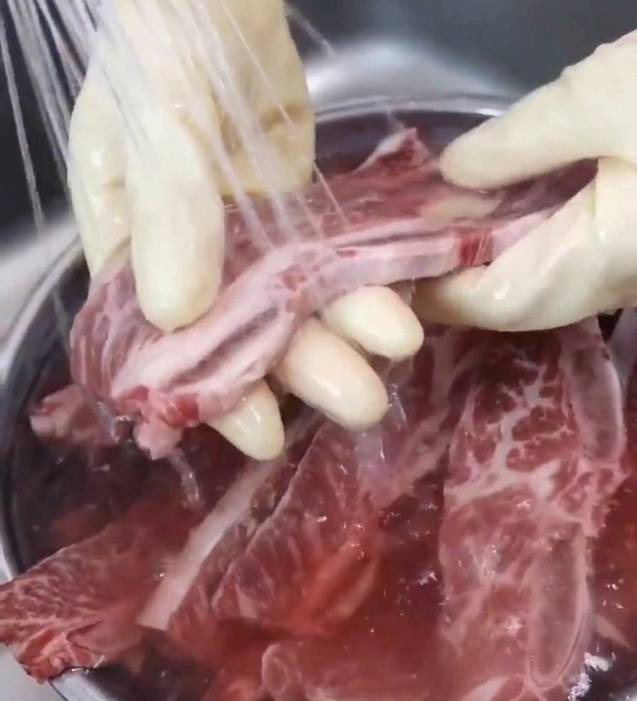 Una mano sciacqua una costina di manzo sotto lacqua corrente del rubinetto della cucina.