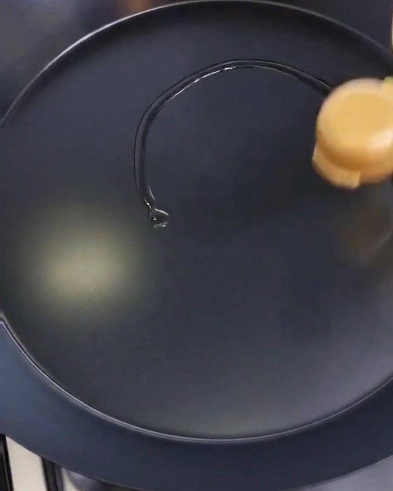 Stesura di un velo dolio su una padella nera circolare con della carta assorbente.