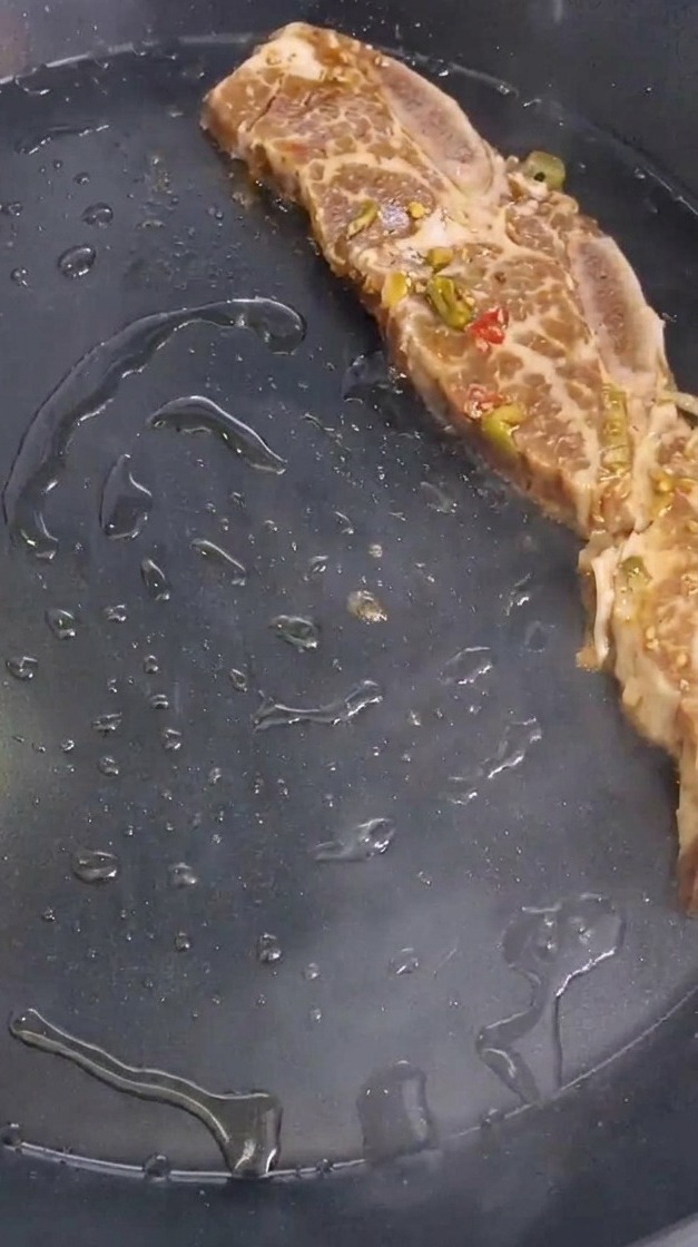 Una costina marinata con pezzetti di peperoncino e cipolla adagiata in una padella calda.