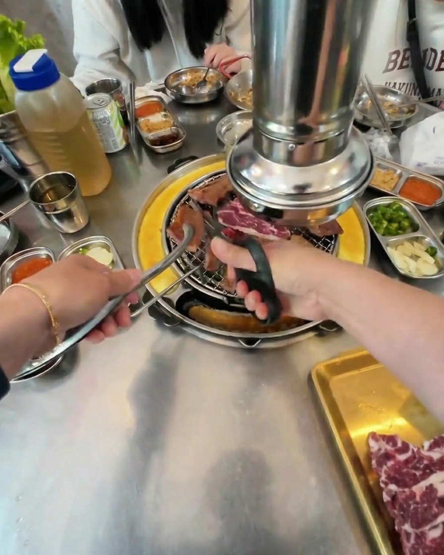 Primo piano di forbici da cucina che tagliano il manzo grigliato in piccoli pezzi quadrati sopra i carboni ardenti.