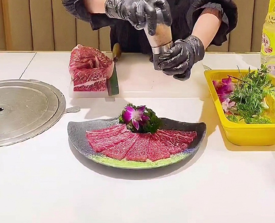 Un macina-sale utilizzato per distribuire cristalli di sale rosa su una composizione decorativa di fette di manzo marezzato crudo.