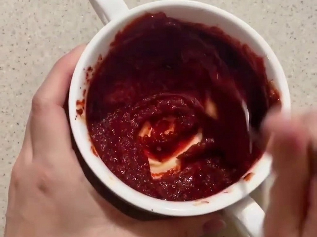 Una persona che mescola una salsa densa di colore rosso scuro a base di gochujang in una piccola ciotola bianca.