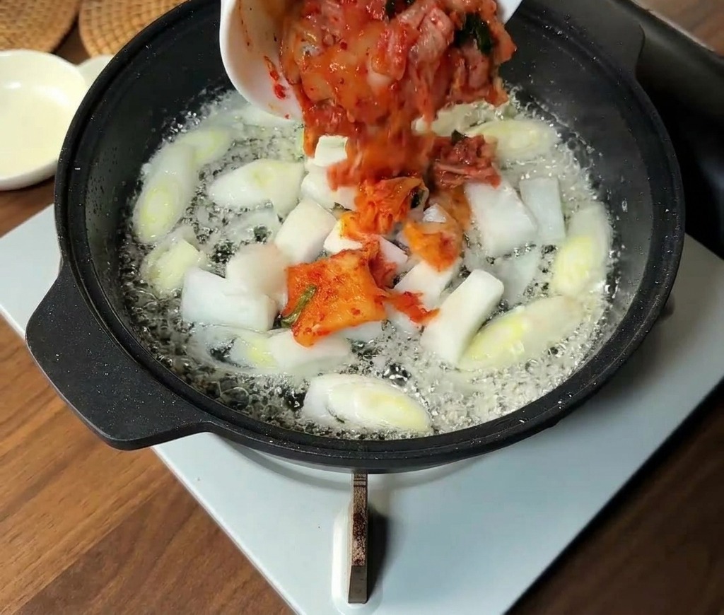Kimchi coreano tritato e fette di cipolla bianca aggiunti alla padella con i cipollotti soffritti.