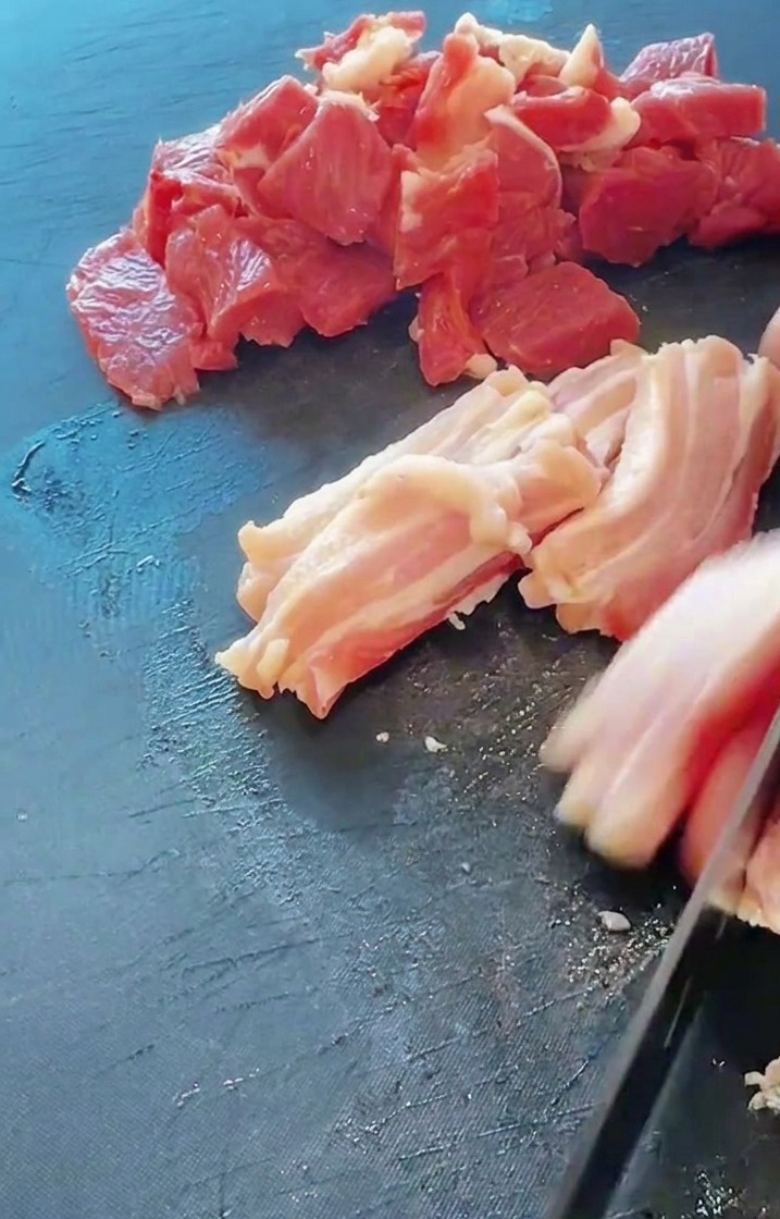 Primo piano di un coltello che affetta fette di pancetta di maiale fresca su un tagliere scuro.