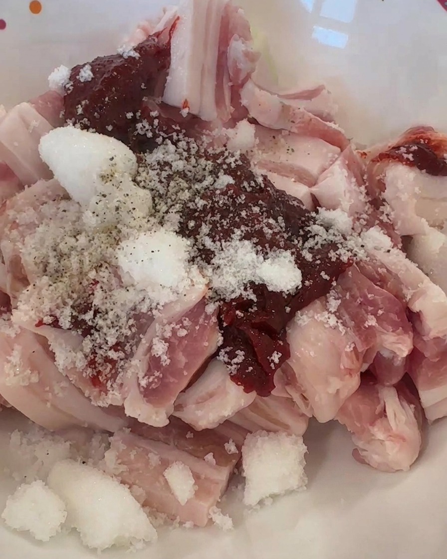 Strisce di maiale crudo in una ciotola con pasta di peperoncino rossa, zucchero bianco e pepe nero macinato.