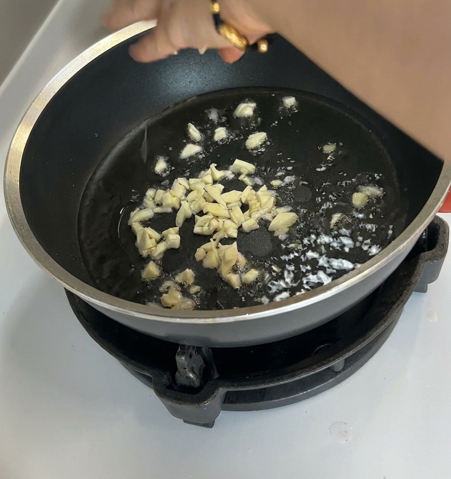 Pezzetti di aglio tritato che sfrigolano nellolio sul fondo di una padella antiaderente scura.