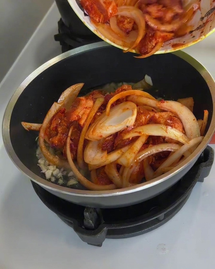 Maiale piccante e cipolle che cuociono in padella, con vapore che sale e la salsa che bolle densa.
