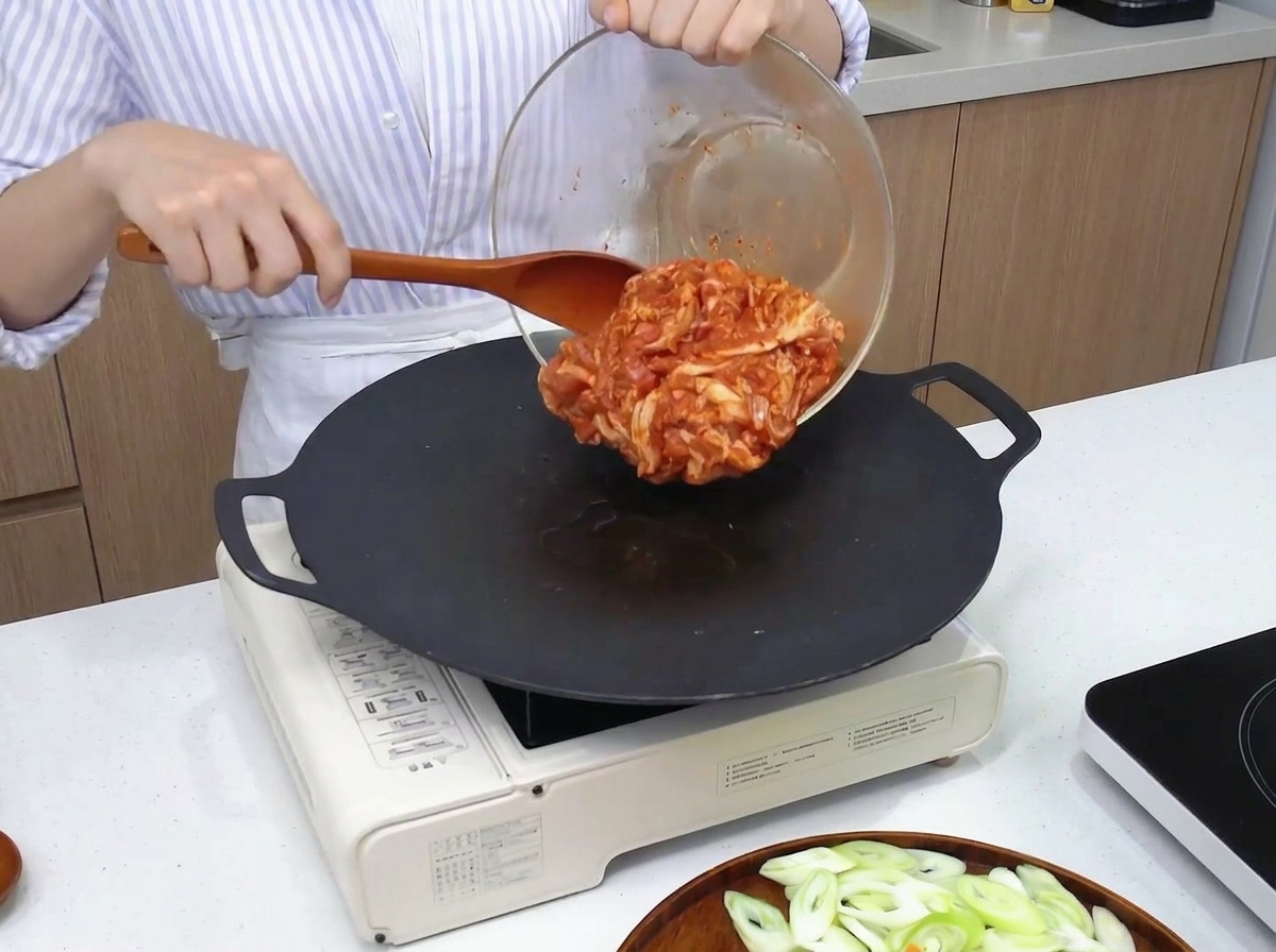 Pancetta di maiale marinata rossa trasferita da una ciotola di vetro a una piastra nera calda tramite una spatola di legno.