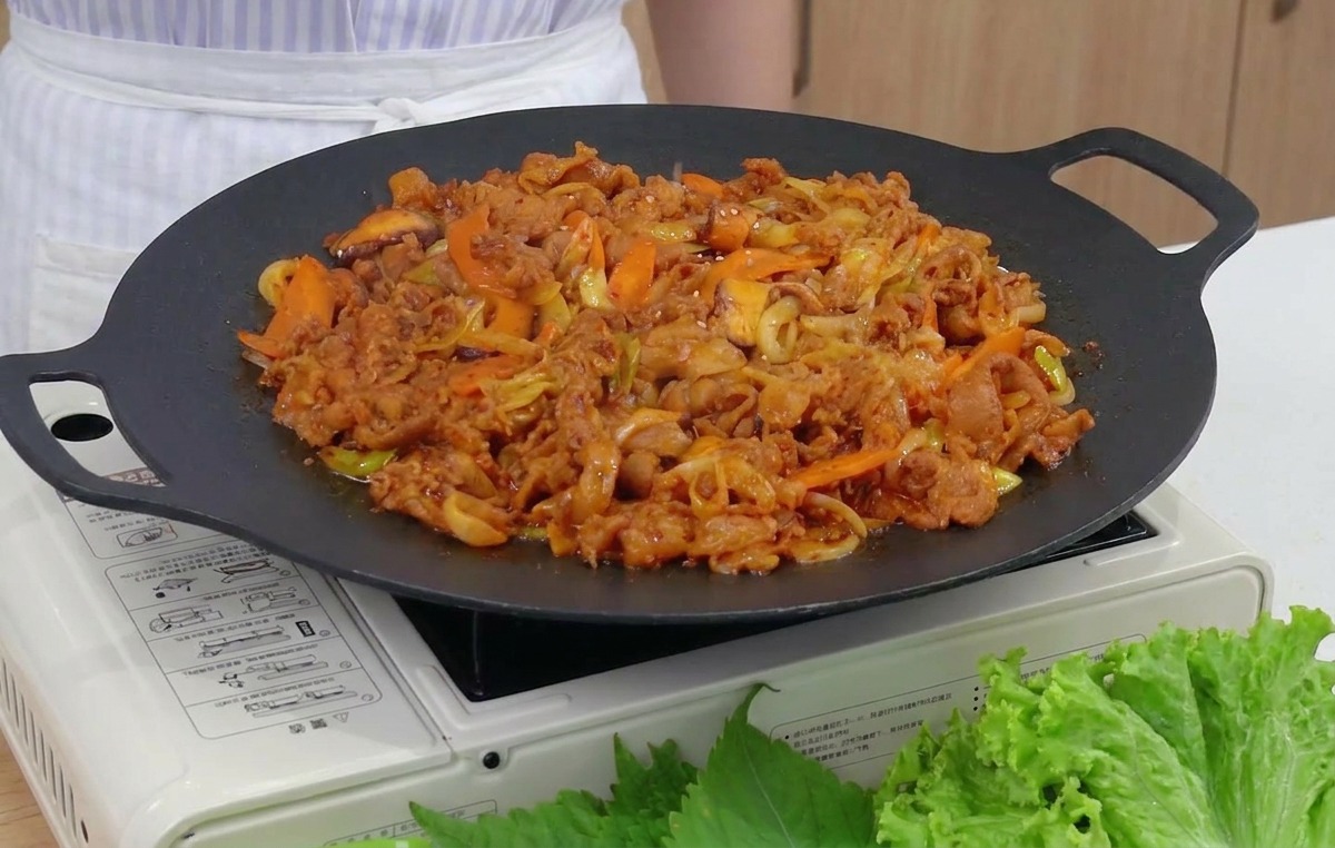 Un primo piano di semi di sesamo tostati sparsi su una padella fumante di maiale e verdure rossi e piccanti.