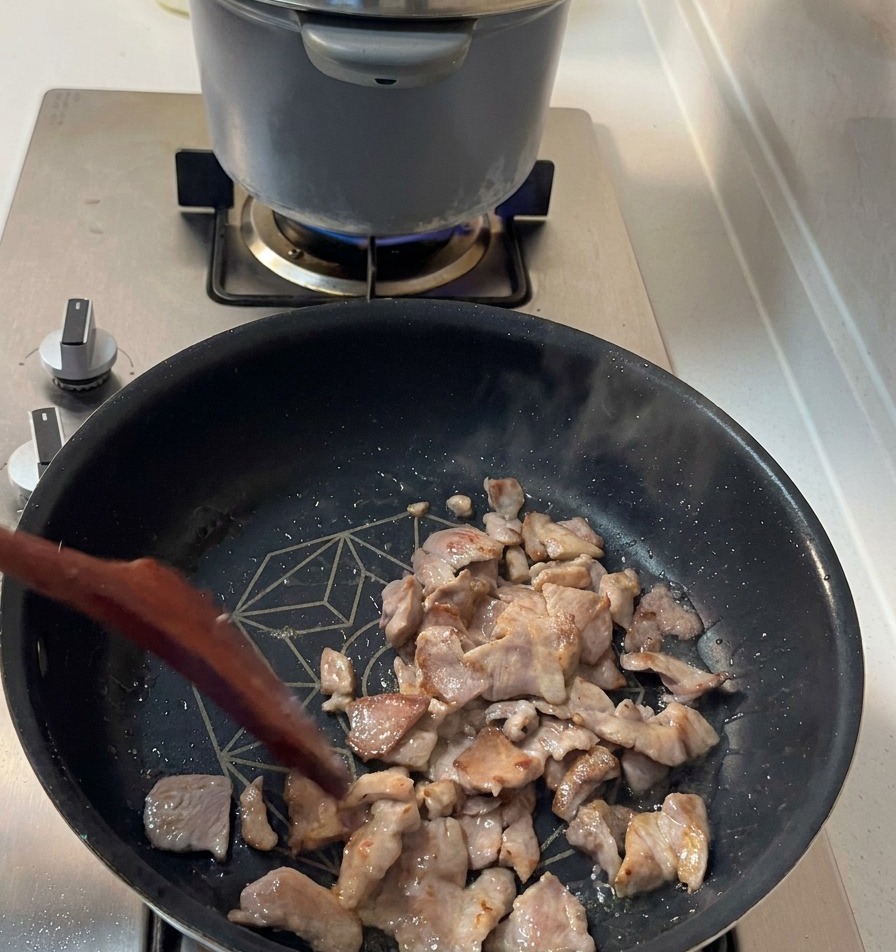 Pezzi sfrigolanti di spalla di maiale con i bordi dorati vengono mescolati in una padella scura.