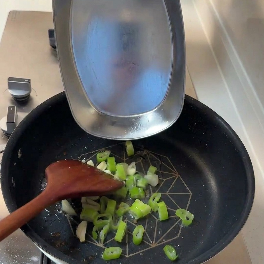 Cipollotti tritati e spicchi daglio affettati vengono aggiunti in una padella con olio di cottura residuo.