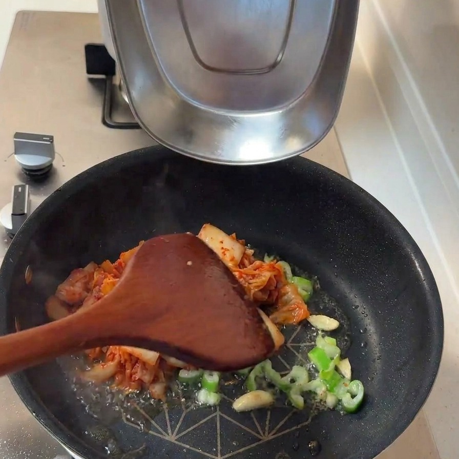 Kimchi fermentato e grosse fette di cipolla bianca vengono aggiunti alla padella con gli aromi soffritti.