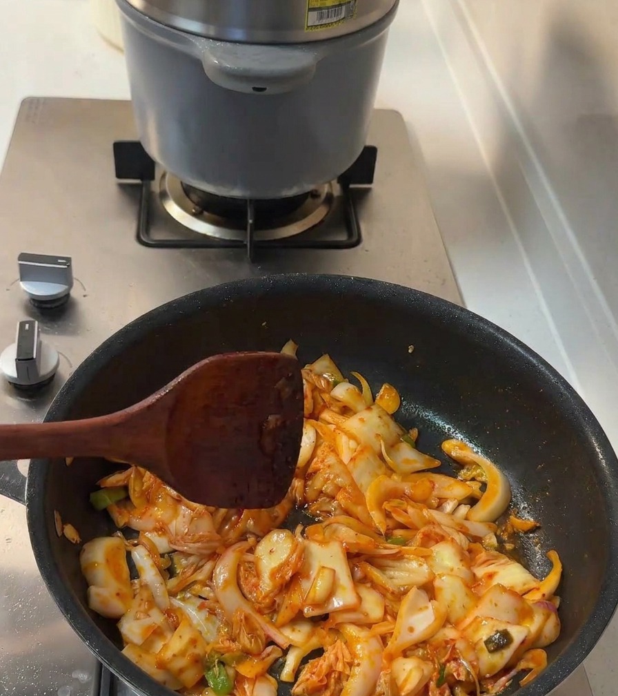 Condimento liquido e zucchero semolato vengono mescolati al kimchi e alle cipolle in padella.