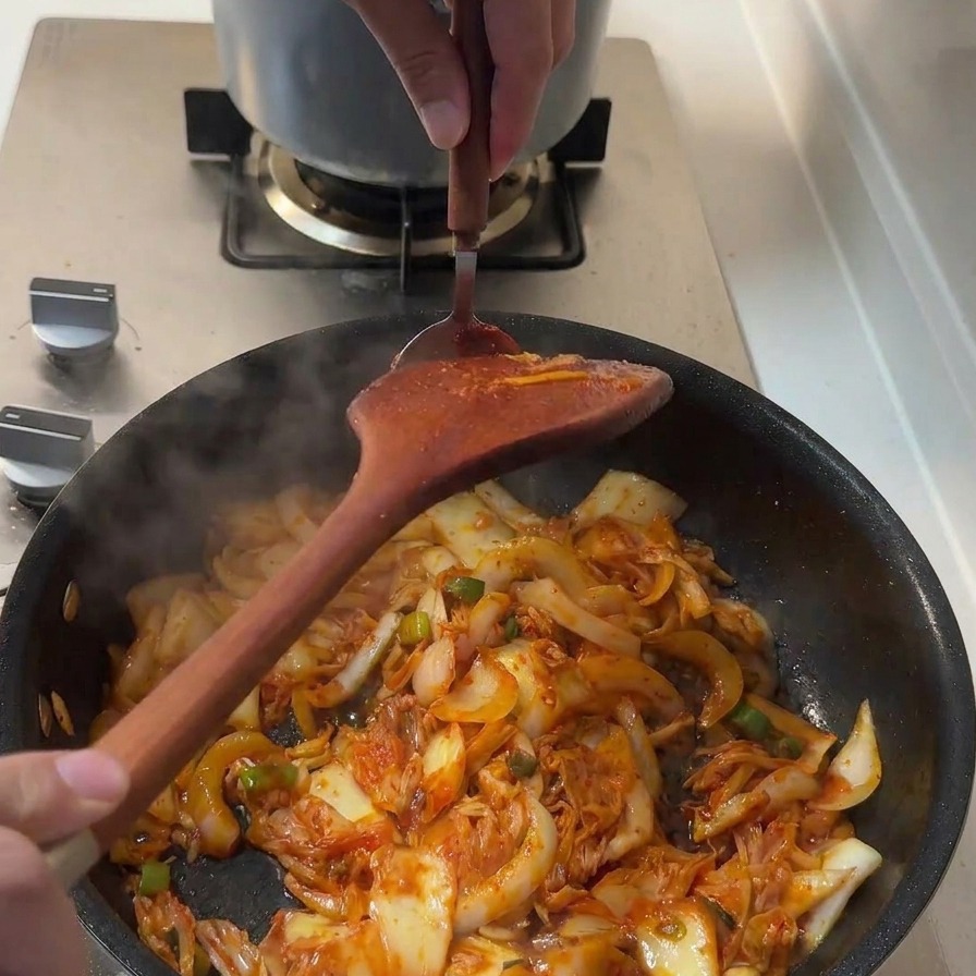 Un cucchiaio di densa pasta gochujang rossa viene aggiunto alla padella con gli ingredienti che saltano.