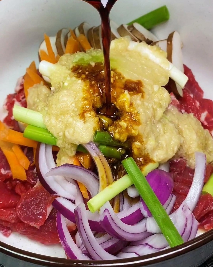Liquido scuro della marinata versato su carne cruda e verdure sormontate da una purea di frutta in una ciotola bianca.