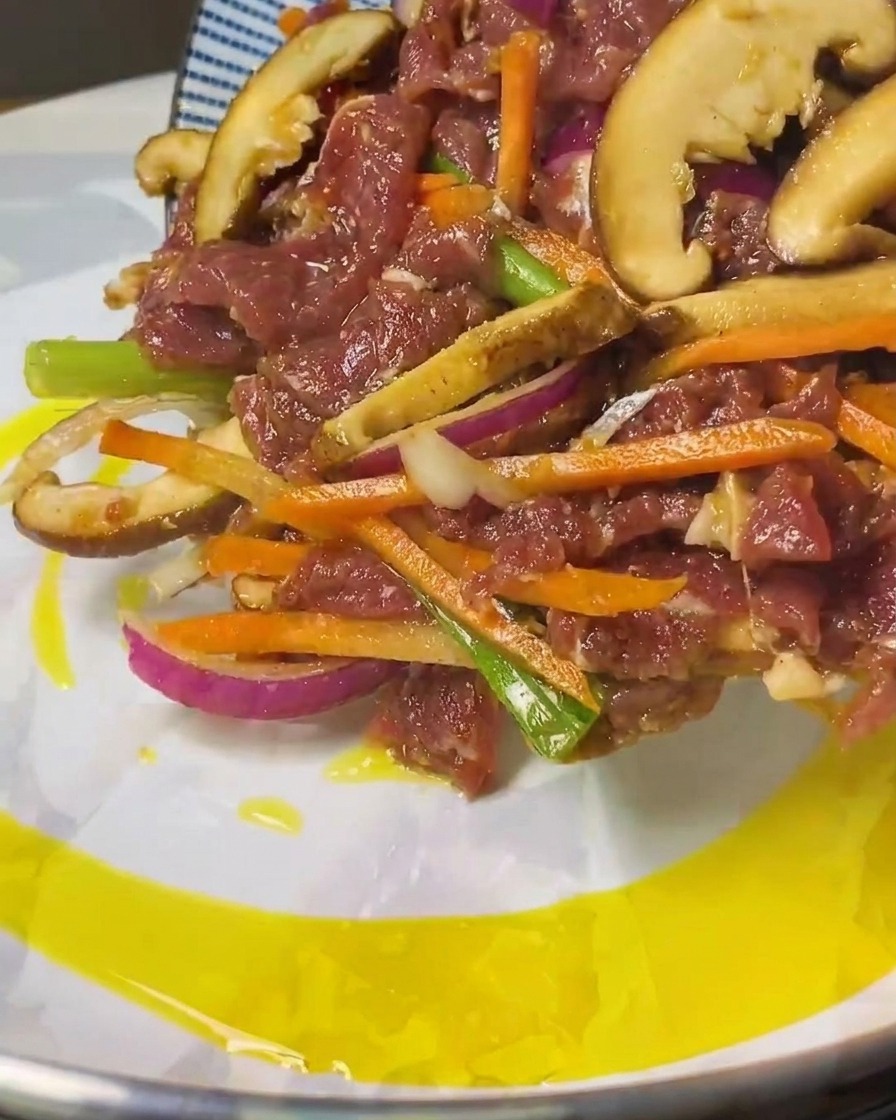 Striscioline di manzo e verdure marinate che scivolano da un piatto blu in una padella con olio caldo.