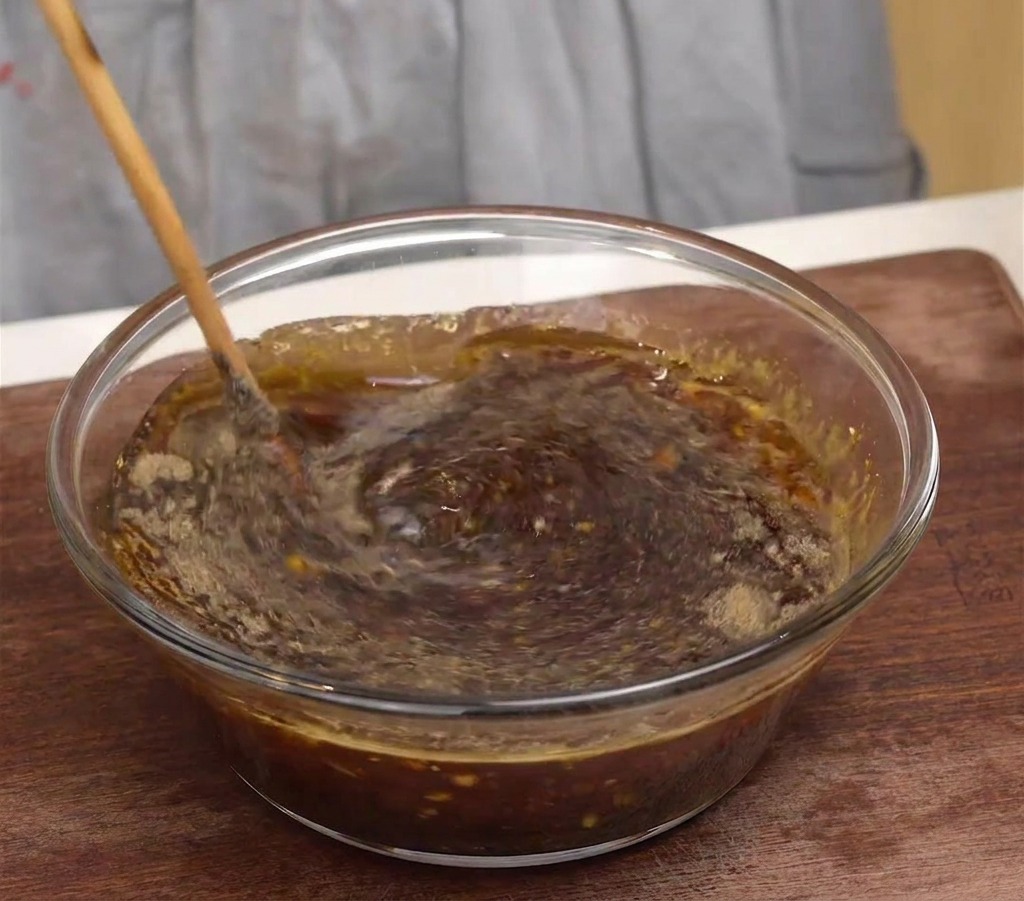 Un cucchiaio di legno che mescola una marinata di manzo coreana scura e aromatica in una ciotola di vetro trasparente.