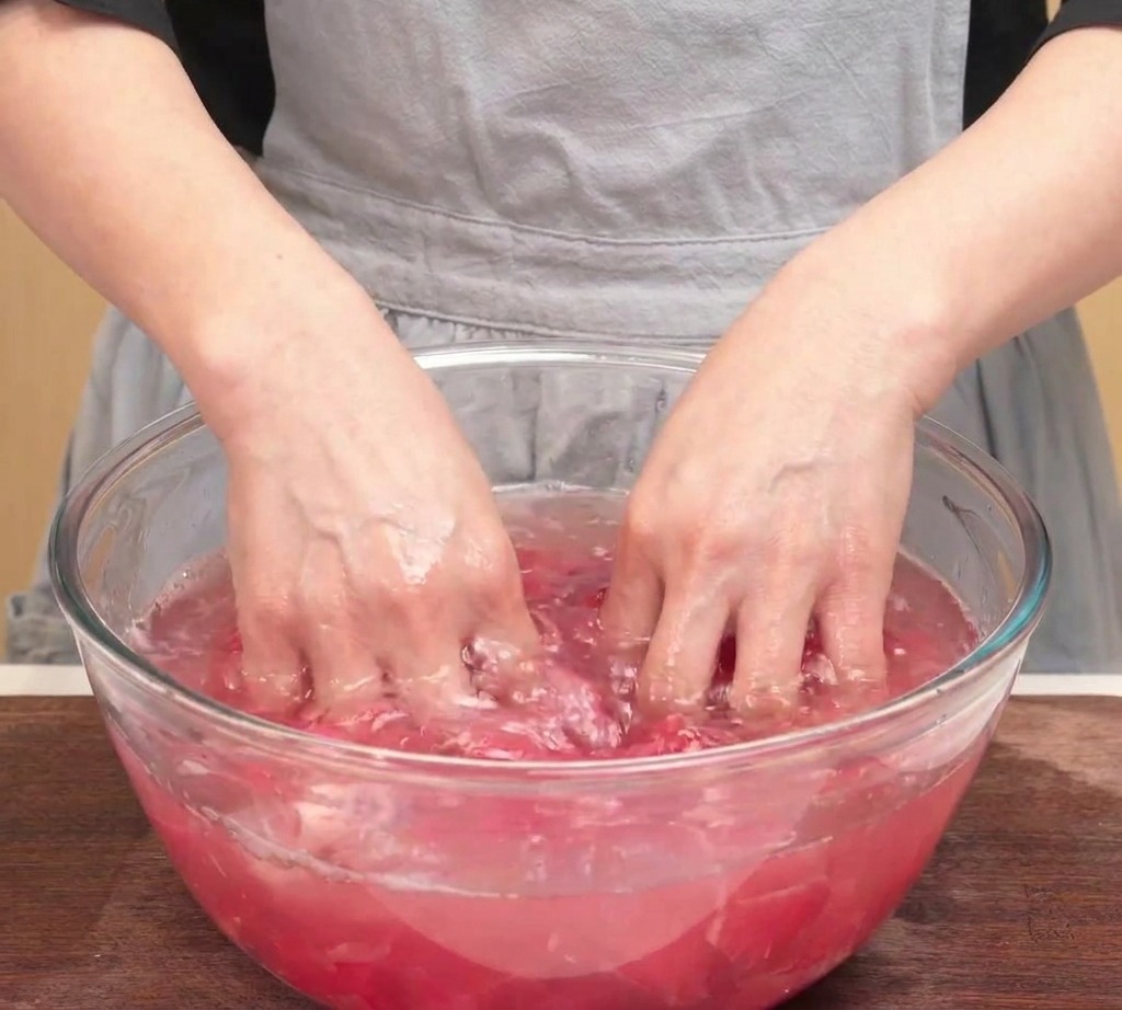 Mani che strizzano un gruppo di fettine di manzo crudo su una ciotola di vetro per rimuovere lacqua in eccesso.