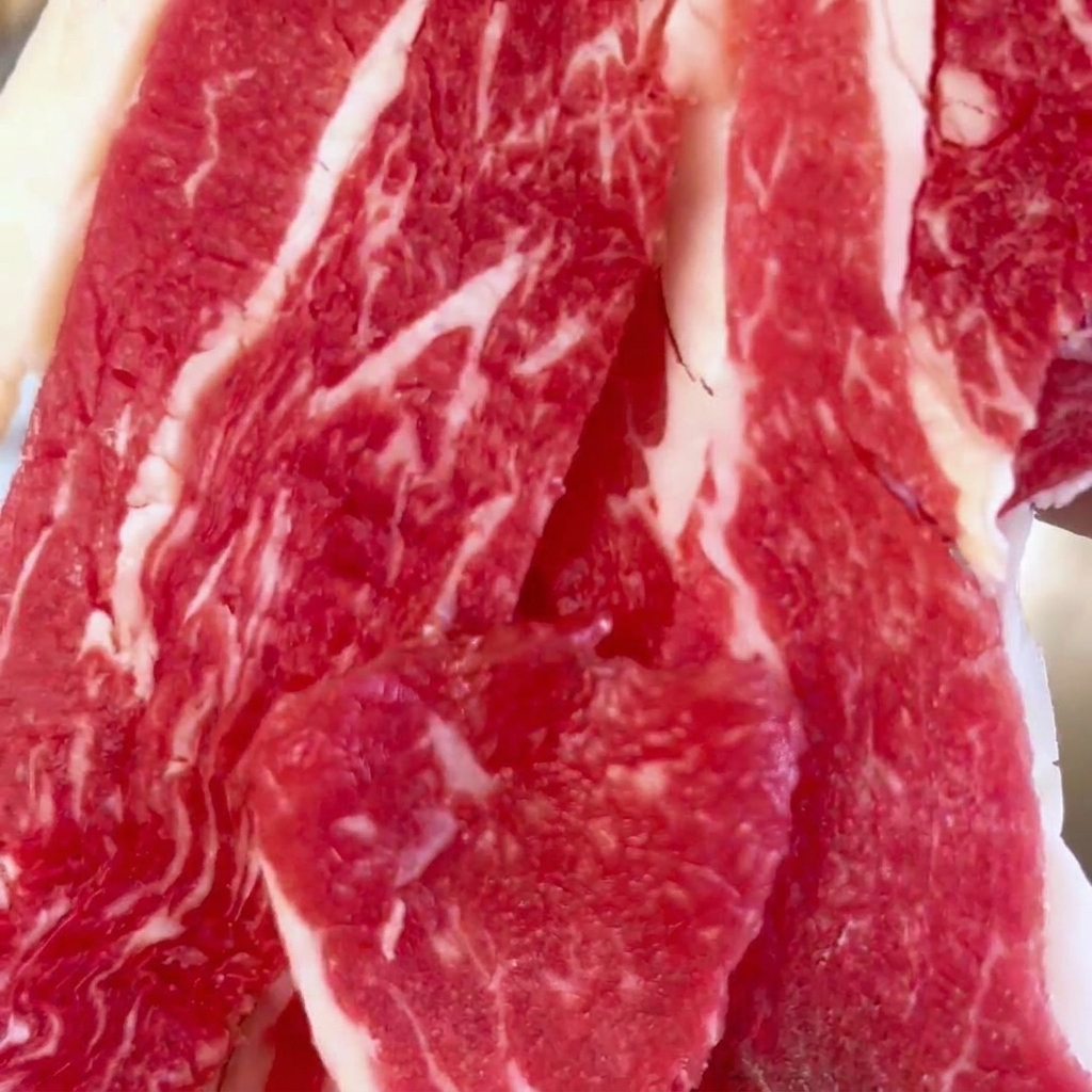 Primo piano di fette di manzo crudo marmorizzato in una ciotola di acciaio inossidabile.
