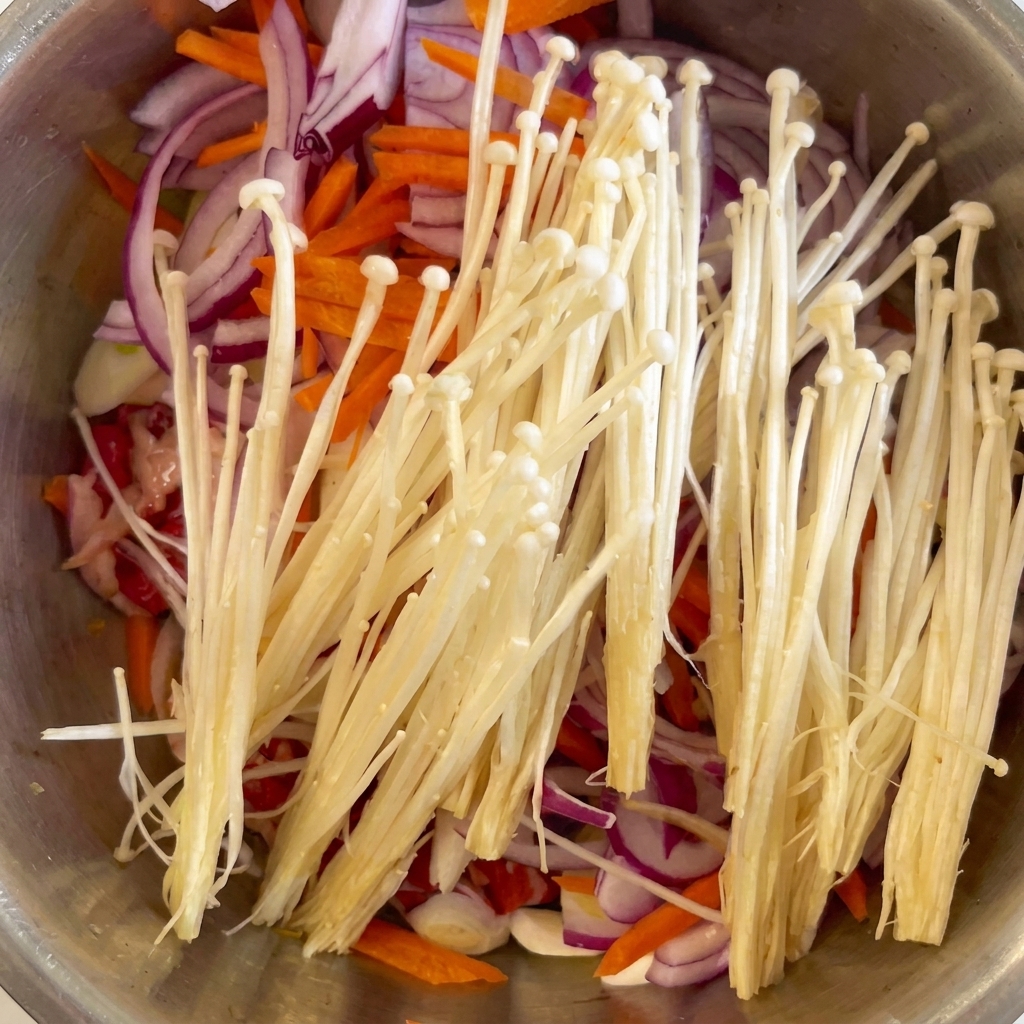 Funghi enoki freschi e aglio tritato posizionati sopra il manzo, le cipolle e le carote.