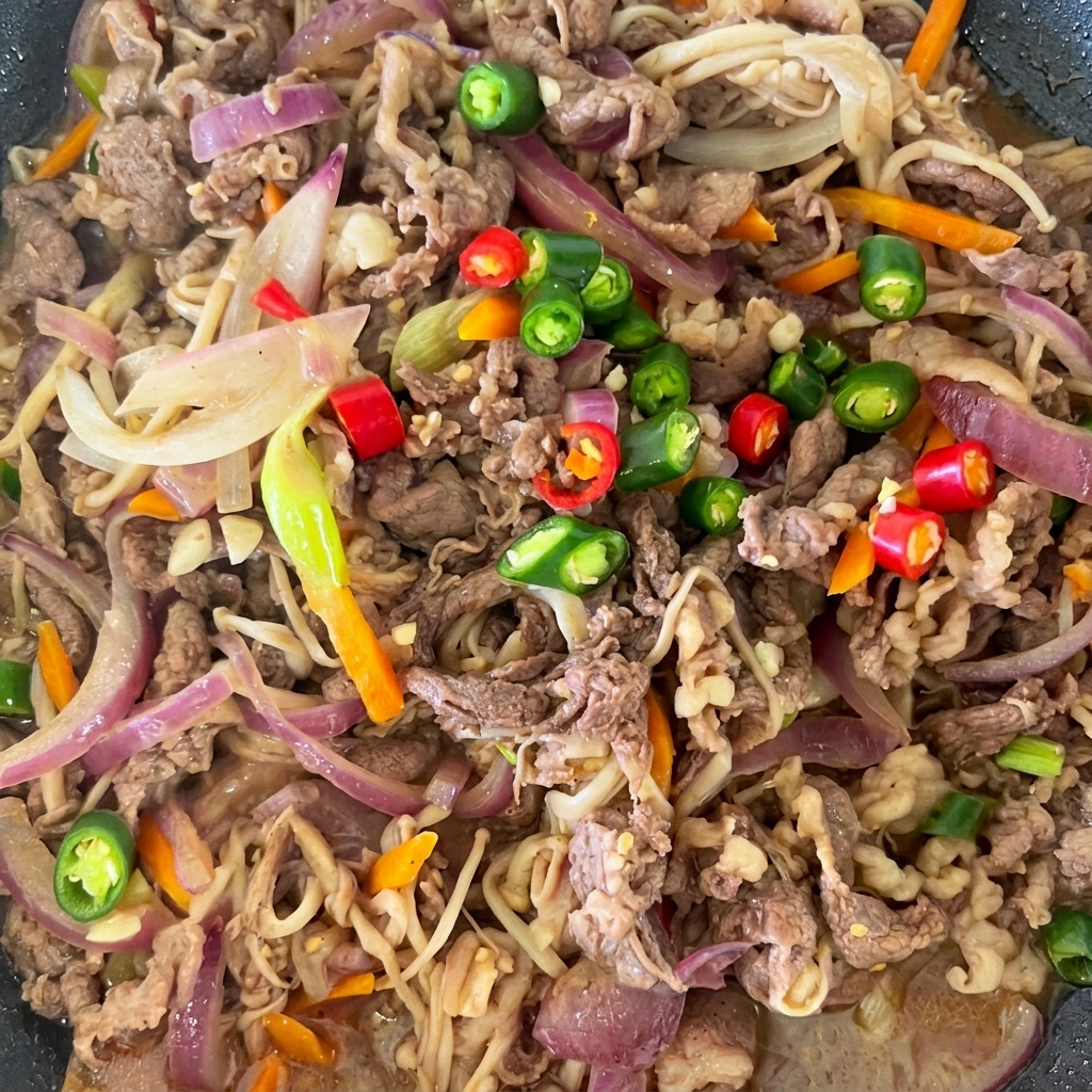 Peperoncini freschi rossi e verdi affettati sopra il bulgogi di manzo cotto in padella.