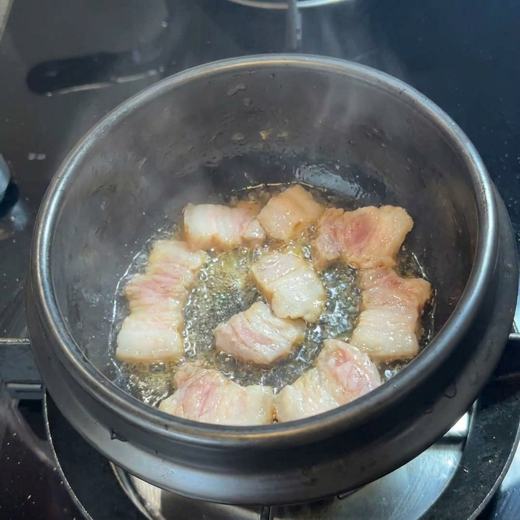 Fette di pancetta di maiale che sfrigolano nel proprio grasso sul fondo di una pentola di pietra nera.