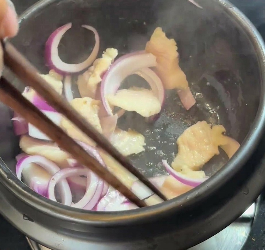 Fette di cipolla rossa fresca mescolate alla pancetta e al grasso fuso in una pentola.