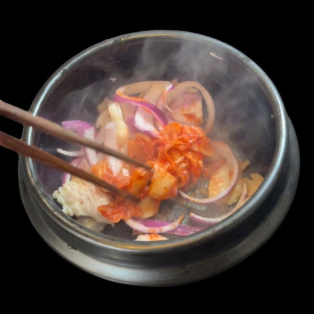 Una manciata di kimchi rosso tritato aggiunta al maiale e alle cipolle nella pentola di pietra.