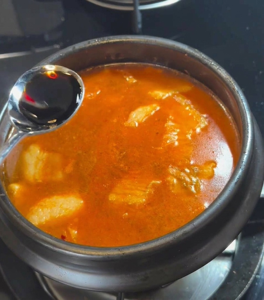 Un cucchiaio dargento che versa salsa di soia scura nel brodo rosso che ribolle.
