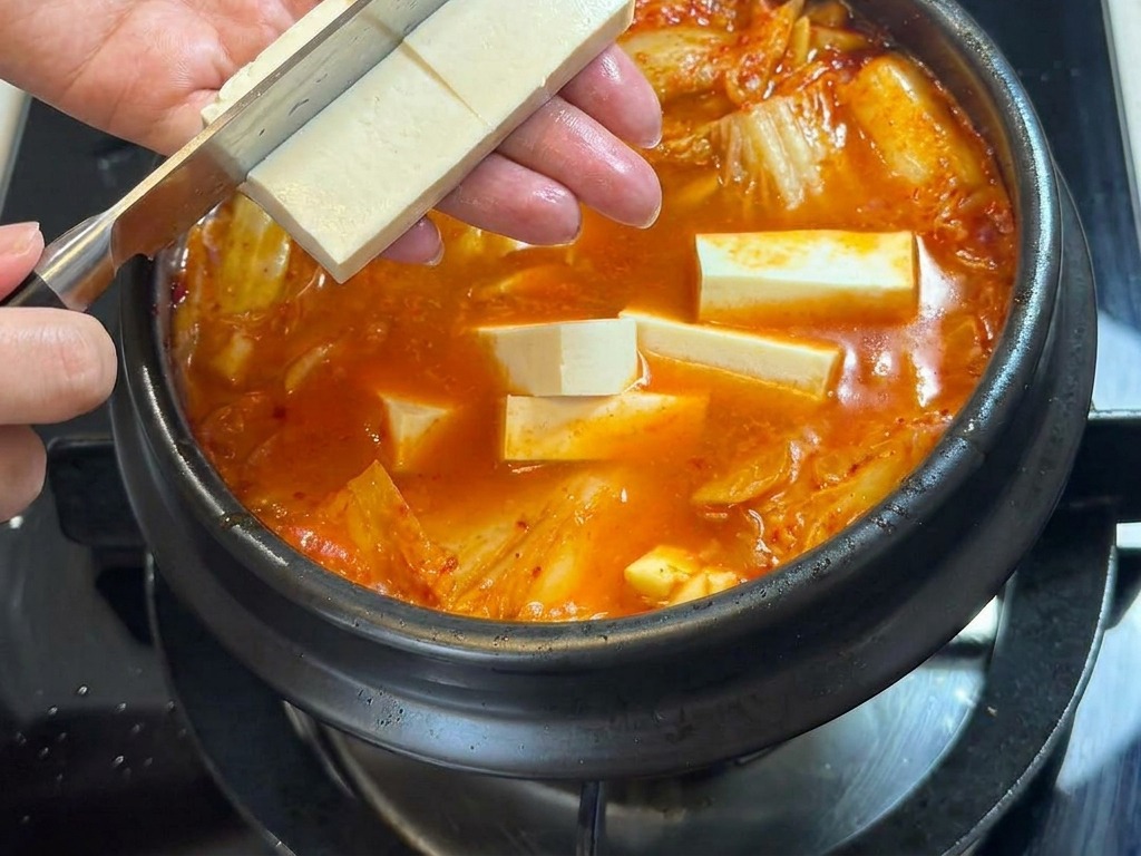 Una persona che taglia un panetto di tofu bianco direttamente sopra la pentola di zuppa piccante.