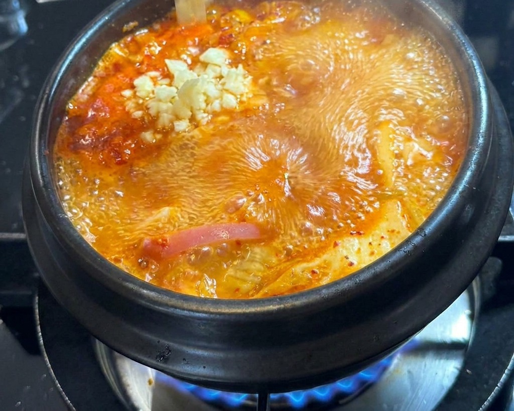 Aglio fresco tritato che cade in una pentola bollente di zuppa rossa.