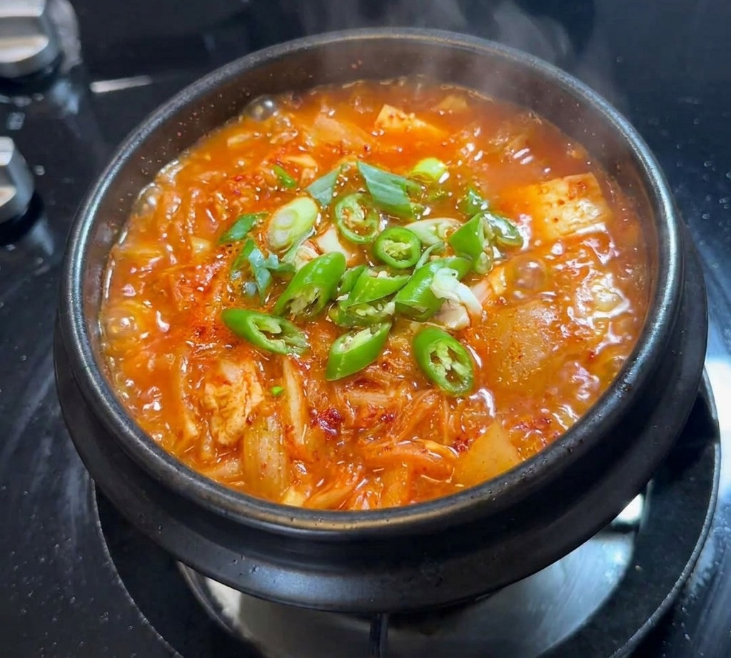 Peperoncini verdi freschi a fette e cipollotti sparsi sulla superficie della zuppa di kimchi.
