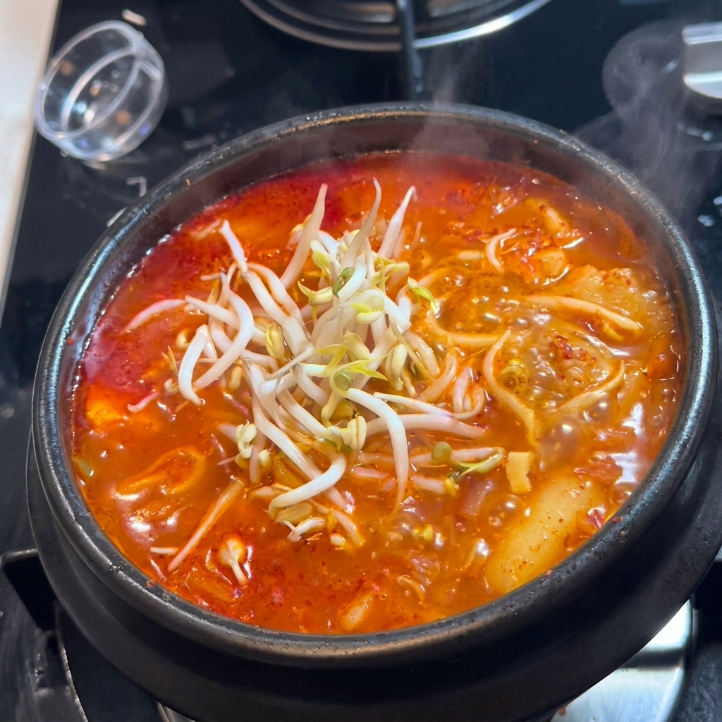 Una manciata di germogli di soia bianchi e freschi posti sopra una pentola di zuppa di kimchi.