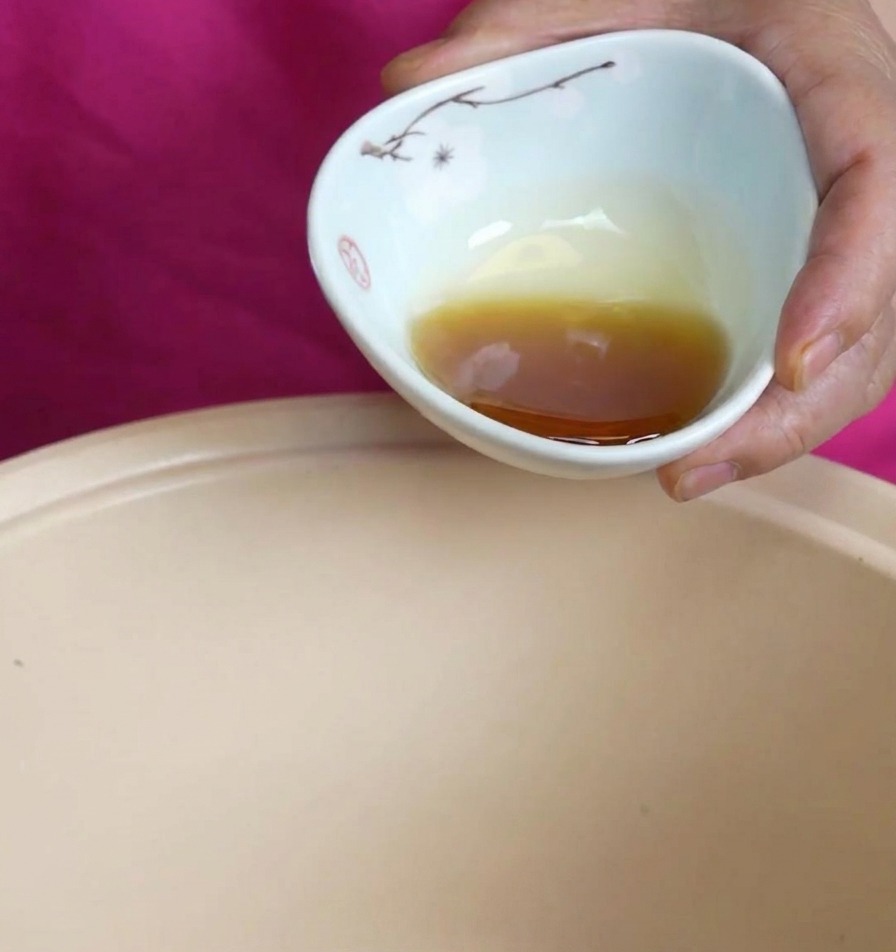 Olio di sesamo ambrato versato da una ciotolina in ceramica in una pentola beige.