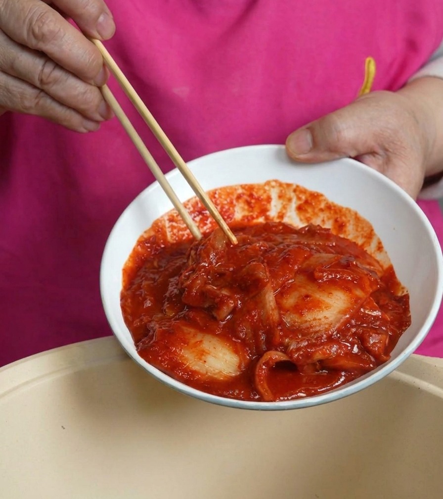 Una ciotola bianca di kimchi rosso e succoso versata nella pentola sopra la carne.