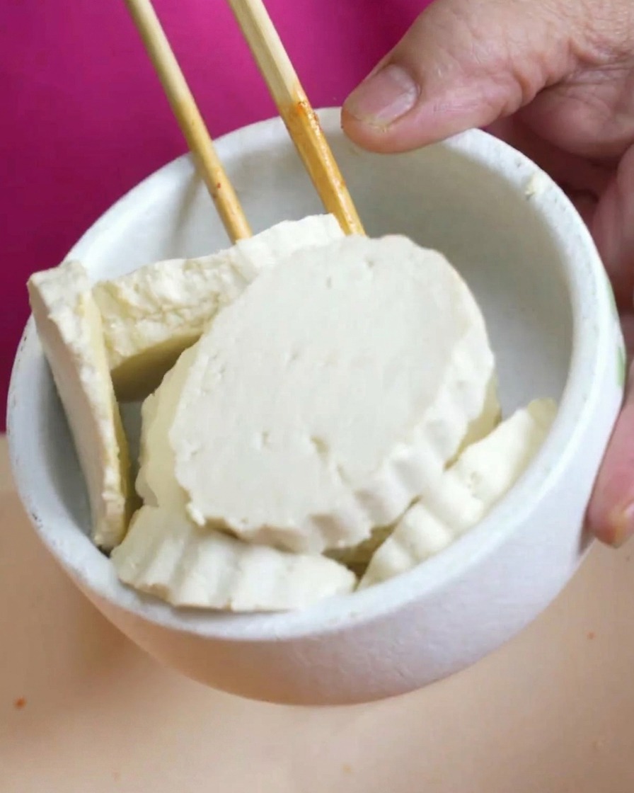 Fette spesse di tofu bianco in una ciotola tenuta sopra la pentola di zuppa fumante.