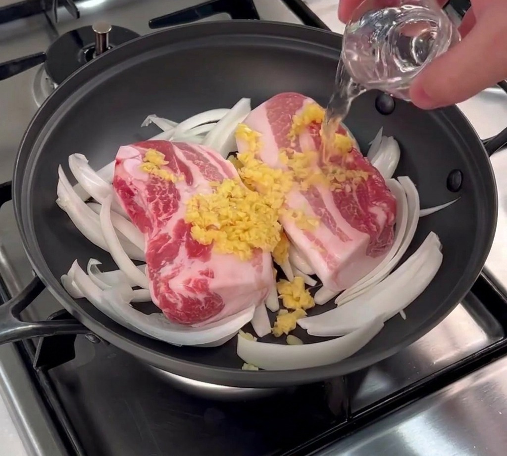 Un bicchierino di vino di riso versato sopra le fette di pancia di maiale ricoperte di aglio.