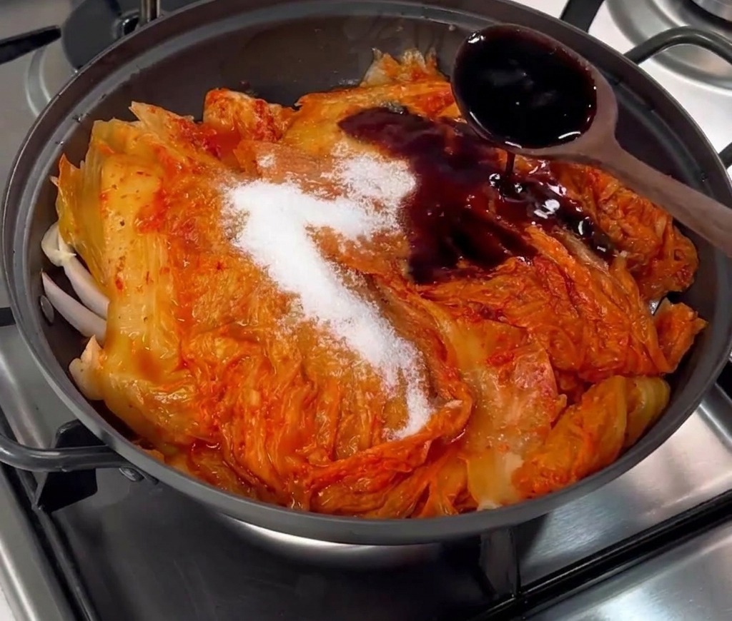 Salsa di soia scura versata da un cucchiaio di legno sopra il kimchi e lo zucchero.