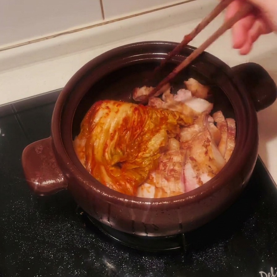 Un intero cespo di kimchi condito e rosso posizionato sopra la pancetta affettata con bacchette di legno.