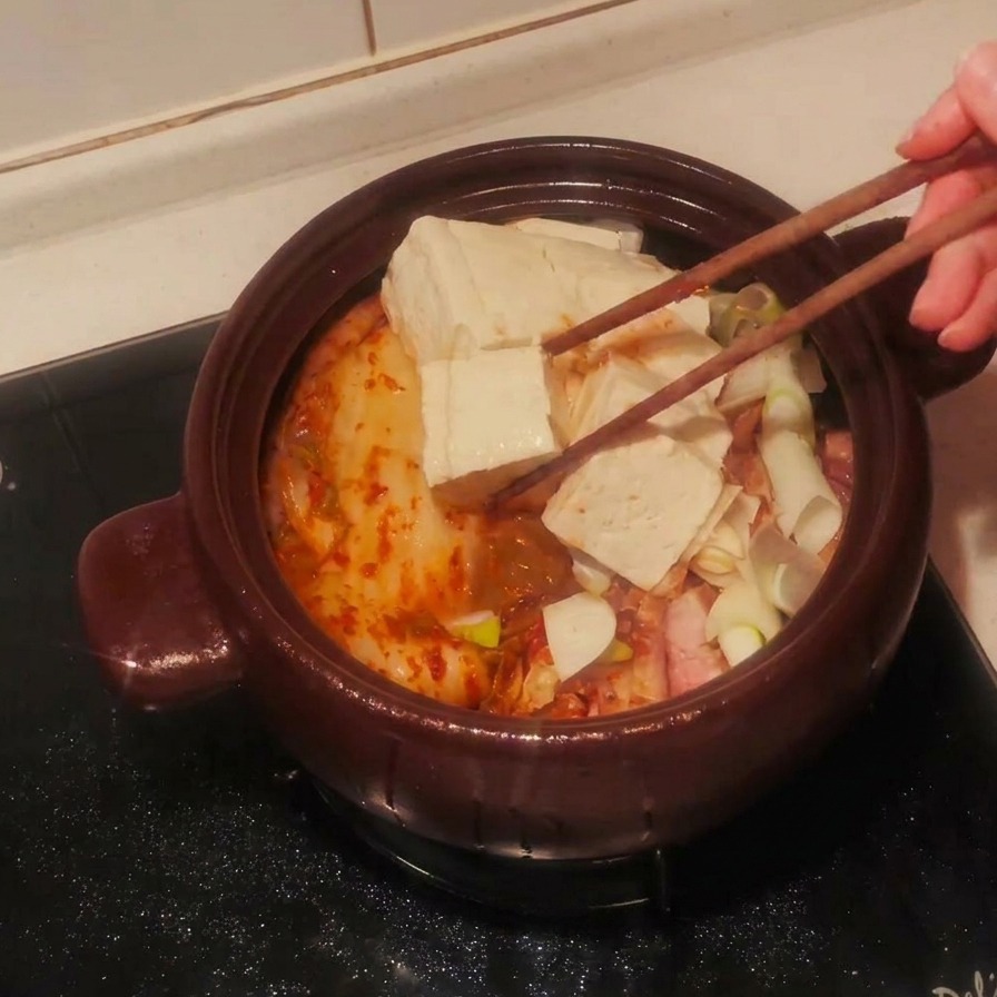 Fette di tofu bianco disposte sopra gli ingredienti dello stufato nella pentola di terracotta con le bacchette.
