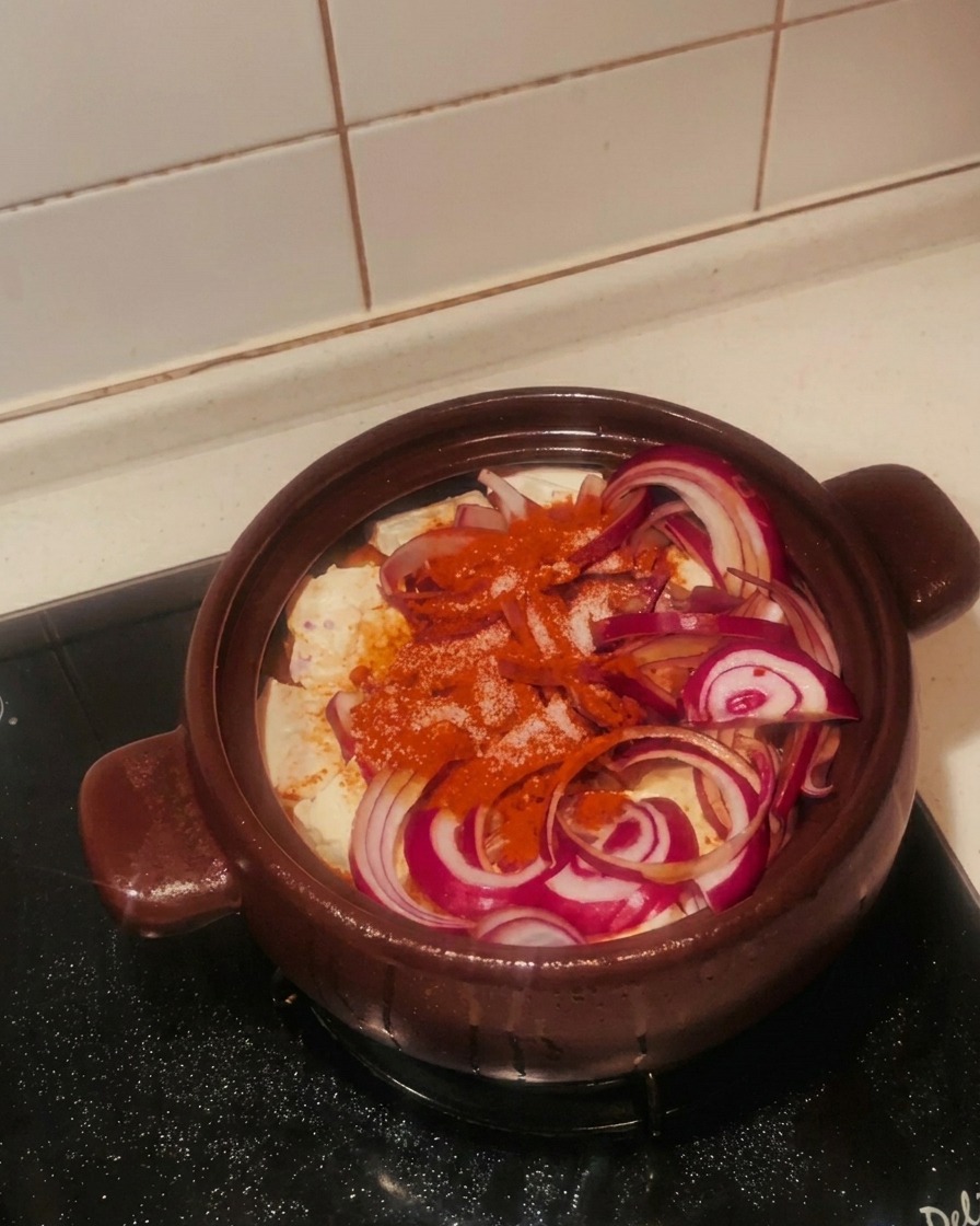 Una mano che spolvera zucchero bianco semolato su cipolle rosse e peperoncino in polvere.