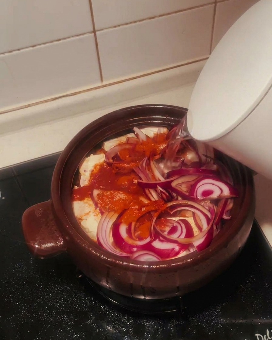 Acqua limpida versata da un bollitore bianco nella pentola piena di kimchi, tofu, cipolle e spezie.