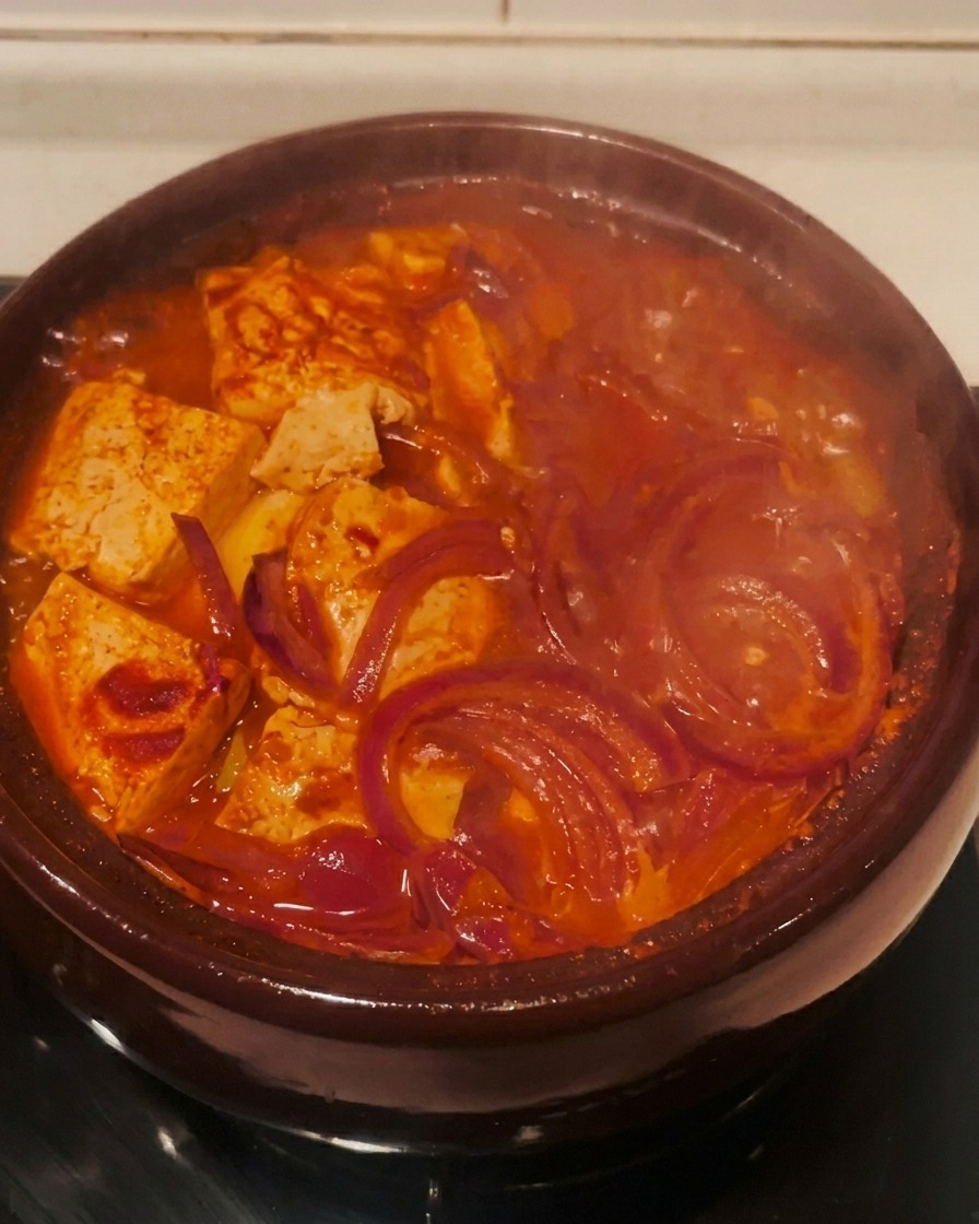 Lo stufato di kimchi rosso che ribolle attivamente nella pentola di terracotta sul fornello.