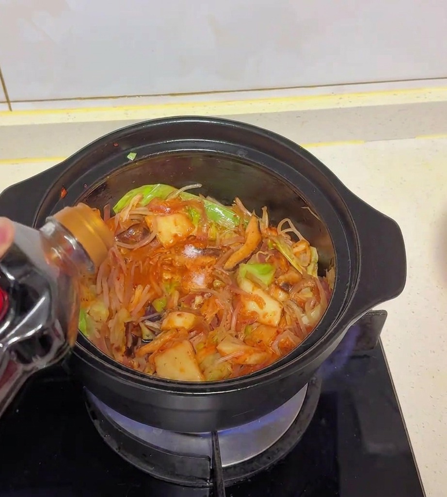 Salsa di soia chiara versata da una bottiglia di plastica scura nella pentola con cavolo, kimchi e funghi.
