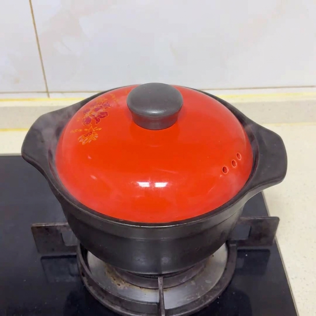 Un coperchio di ceramica rosso acceso copre una pentola nera su un fornello a gas con vapore che fuoriesce.
