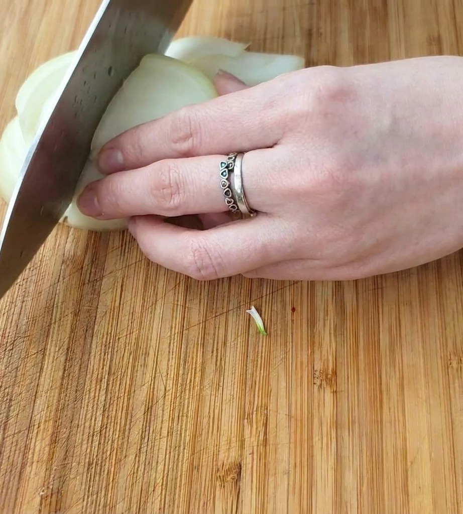 Primo piano di una mano che usa un coltello da chef per tagliare una cipolla bianca a cubetti su un tagliere di legno.