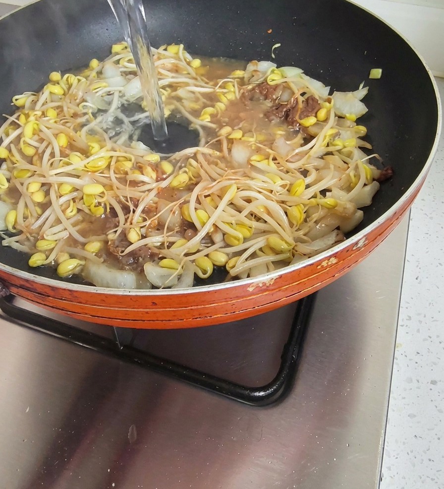 Un getto dacqua limpida versato in una padella contenente germogli e cipolle in una base di pasta di soia.