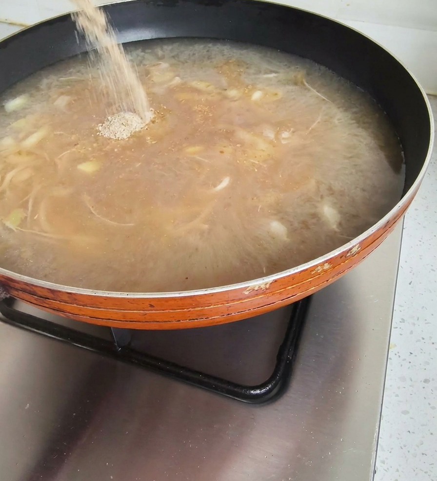 Polvere di condimento versata da una bustina in una padella di brodo marrone bollente sul fornello.