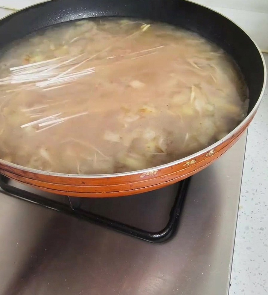 Mani che immergono noodles secchi e trasparenti in una padella di zuppa di soia coreana che sobbolle.
